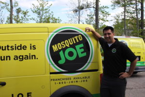 Mosquito Joe Technician wearing black and balck pants posing next Mosquito Joe Van
