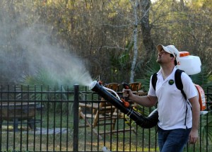 Mosquito Joe Technician wearing white hat with a white shirt and black pants, spraying outdoor yard with barrier treatment spray in Kingwood County
